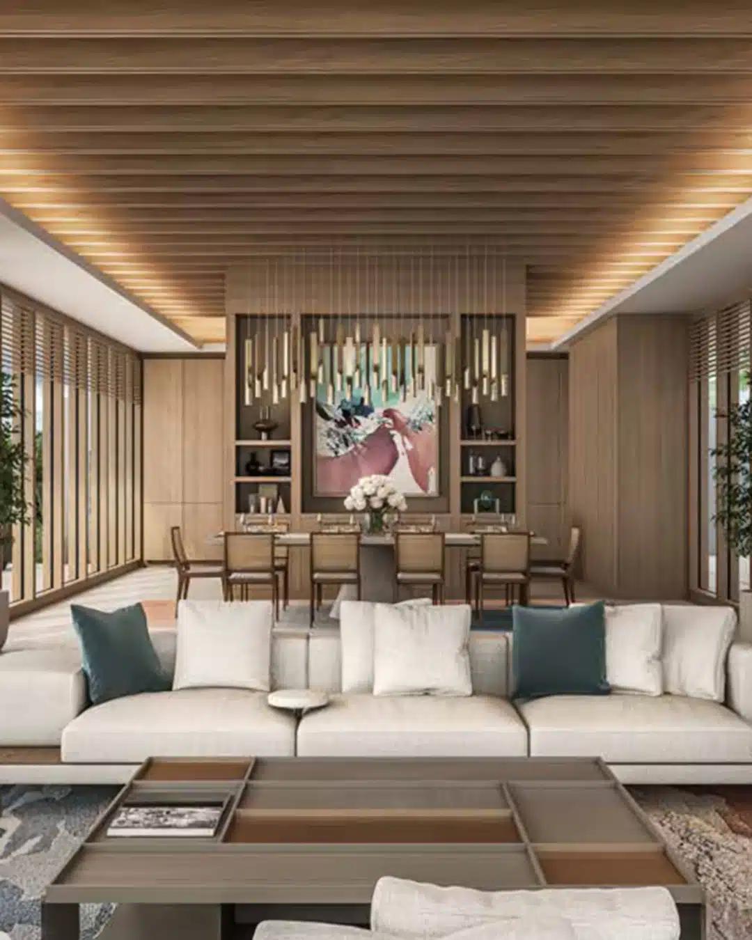 Open-plan living and dining area with a light sofa, teal pillows, and a wooden slatted ceiling; a long dining table under a cluster of pendant lights behind.