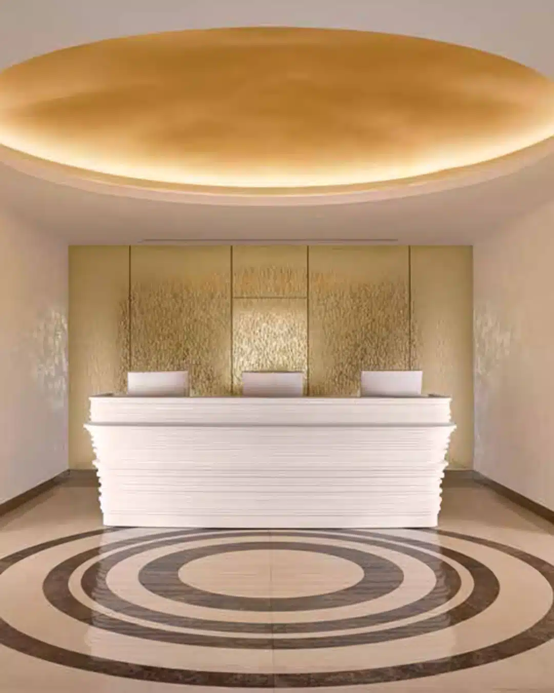 Reception desk in a modern, luxurious lobby with gold textured wall panels and a circular tiled floor pattern.]”,