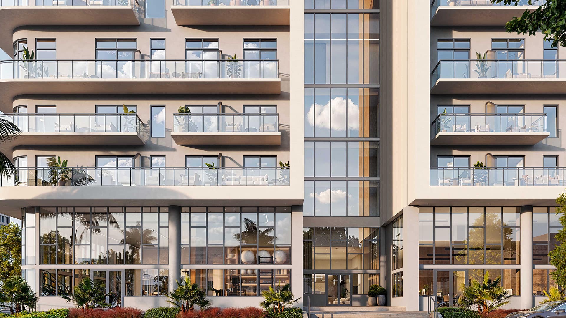 Modern apartment building with glass balconies and large windows reflecting clouds in the sky on a bright day.