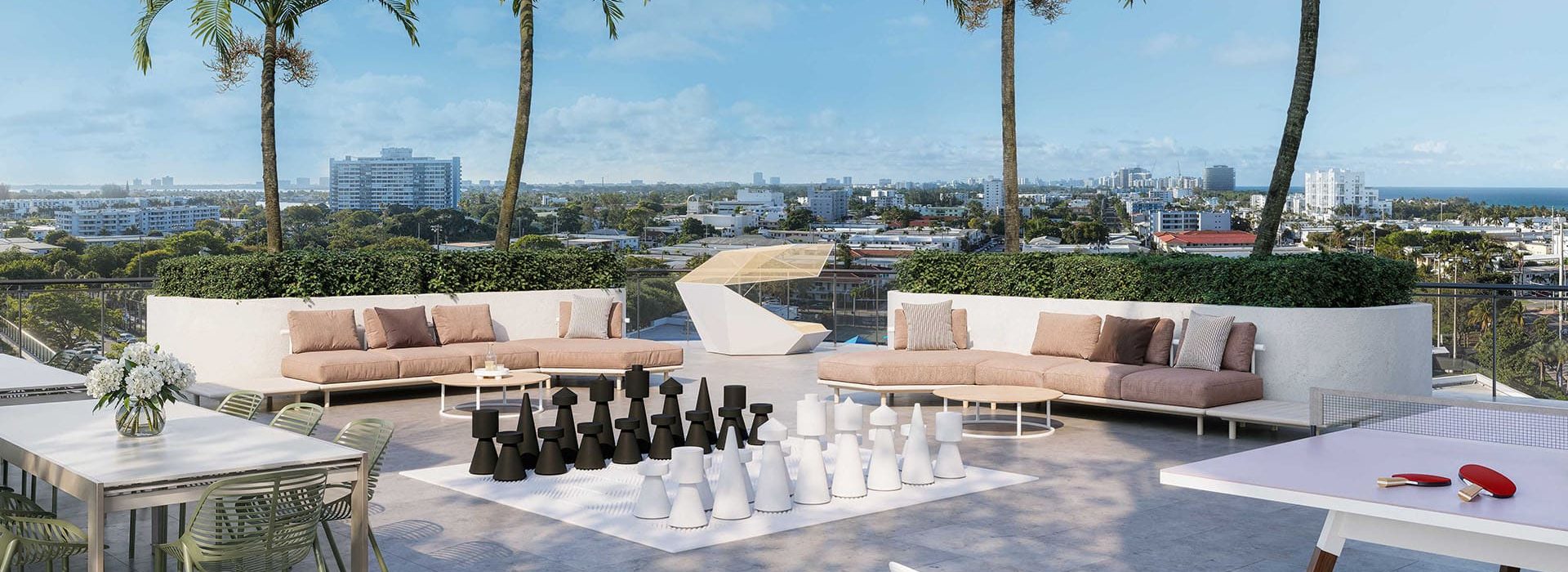 Rooftop lounge with beige sectional seating, palm trees, and a large chessboard, overlooking a city skyline.